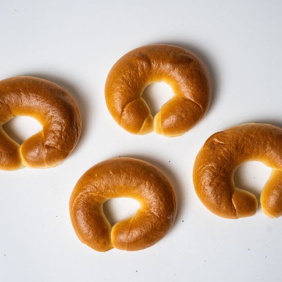 Vier Brezeln sind auf einem weißen Hintergrund zu sehen. Jede Brezel hat ein Loch in der Mitte. Die Brezeln variieren in der Größe und haben eine goldbraune Kruste.