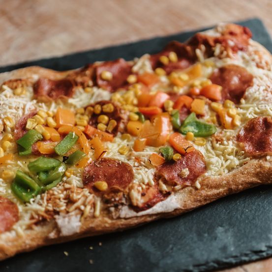 Eine Nahaufnahme einer vegetarischen Pizza mit Pepperoni, Käse, Mais und Paprika auf einer Holzoberfläche.