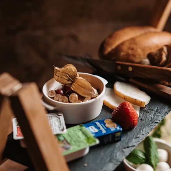 Eine Nahaufnahme eines Holztisches mit einer weißen Schüssel Trauben, einer Erdbeere, Brotscheiben und verschiedenen Gegenständen.