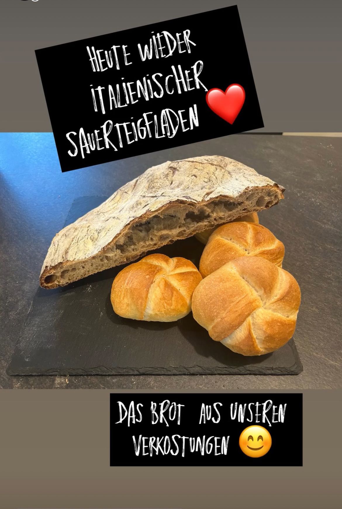 Ein Laib italienischen Sauerteigbrots wird auf einer dunklen Oberfläche zusammen mit drei runden Brötchen präsentiert. Das Bild hat einen schwarzen Rand mit Textüberlagerung.