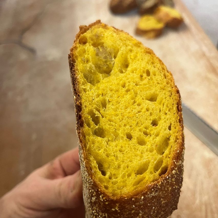 Ein Nahaufnahme eines geschnittenen Stücks Brot mit sichtbarer Krumenstruktur und goldener Kruste. Das Brot hat ein rustikales Aussehen mit einer rauen Textur.