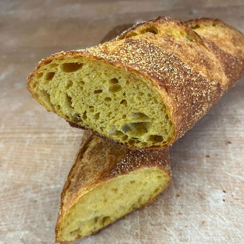 Ein geschnittenes Baguette mit goldener Kruste und luftigem Inneren, bestreut mit Sesamkörnern, liegt auf einer Holzunterlage.