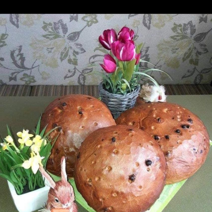 Drei kugelförmige Brote sind mit einer Vase mit rosa Tulpen und einer gelben Narzissenpflanze ausgestellt. Eine kleine Keramikhasenfigur hält eine Karotte.