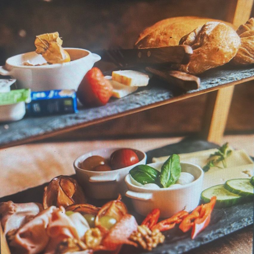 Eine zweistöckige Präsentation von Frühstücksnahrungsmitteln, darunter Bagels, Tomaten, Käse und Brot. Schüsseln mit Basilikum und Mozzarella und eine separate Schüssel mit Trauben.