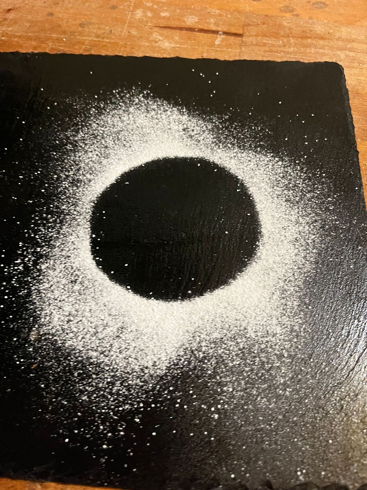 Eine schwarze Oberfläche hat eine kreisförmige weiße Pulverzeichnung in der Mitte mit verstreutem weißem Pulver darum herum.