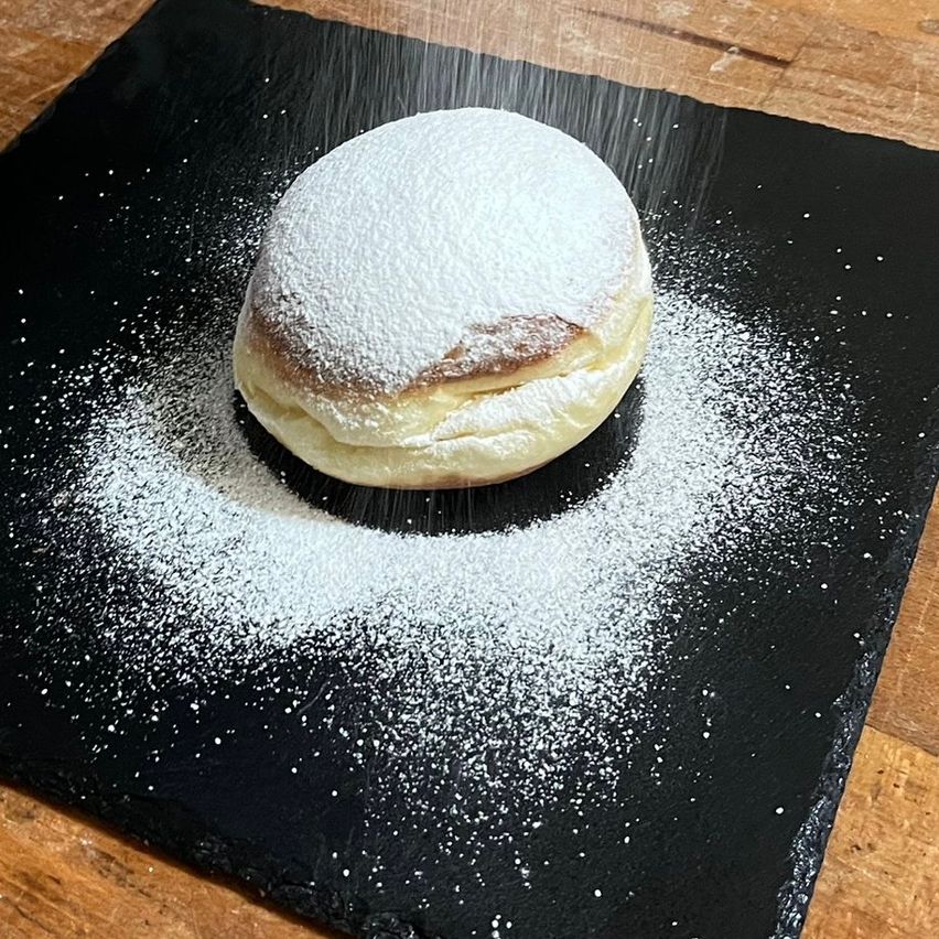 Eine pulverisierte Backware auf einem schwarzen Teller, bestreut mit Puderzucker, und mit Puderzucker auf einer Holzoberfläche bestreut.