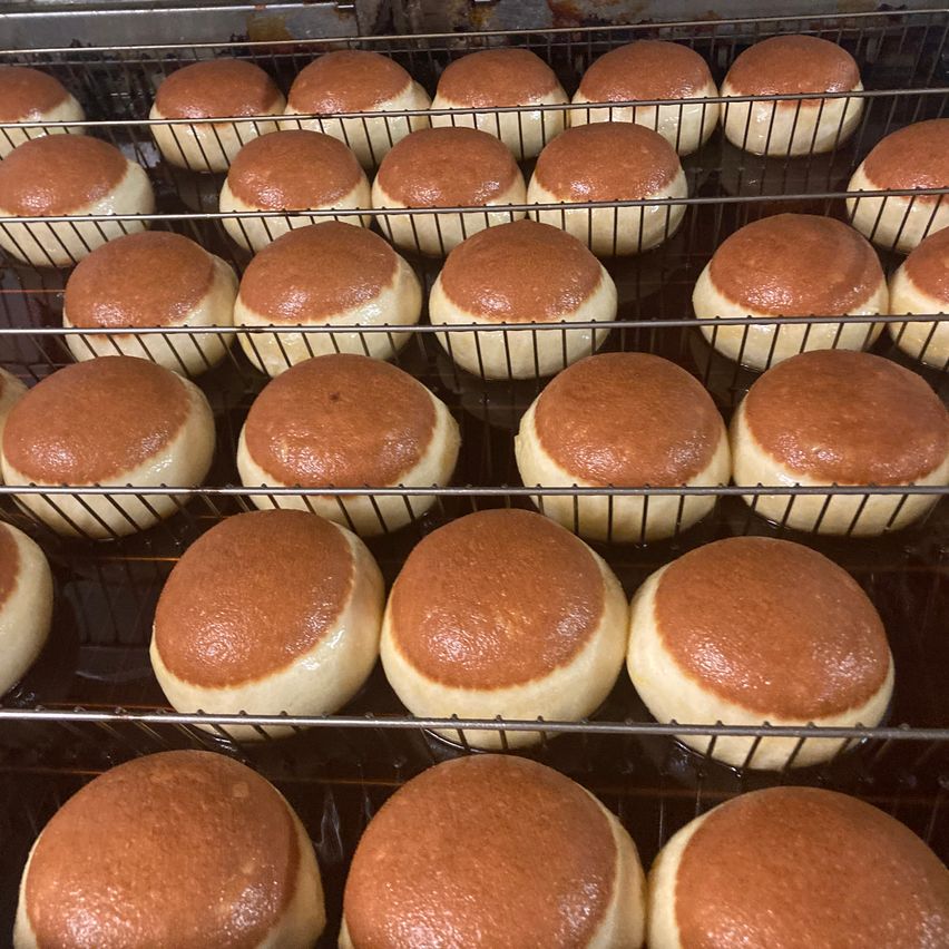 Ein Regal mit mehreren Backblechen von frisch gebackenen Brötchen mit brauner Kruste ist in einem Ofen zu sehen. Die Brötchen sind rund und scheinen gleichmäßig gebacken zu sein.
