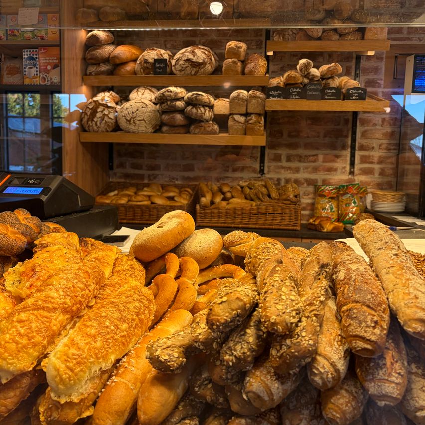 Eine Bäckerei-Auslage mit verschiedenen Brotsorten, darunter Baguettes, Brezeln und Brötchen, auf Regalen und einem Tresen angeordnet.