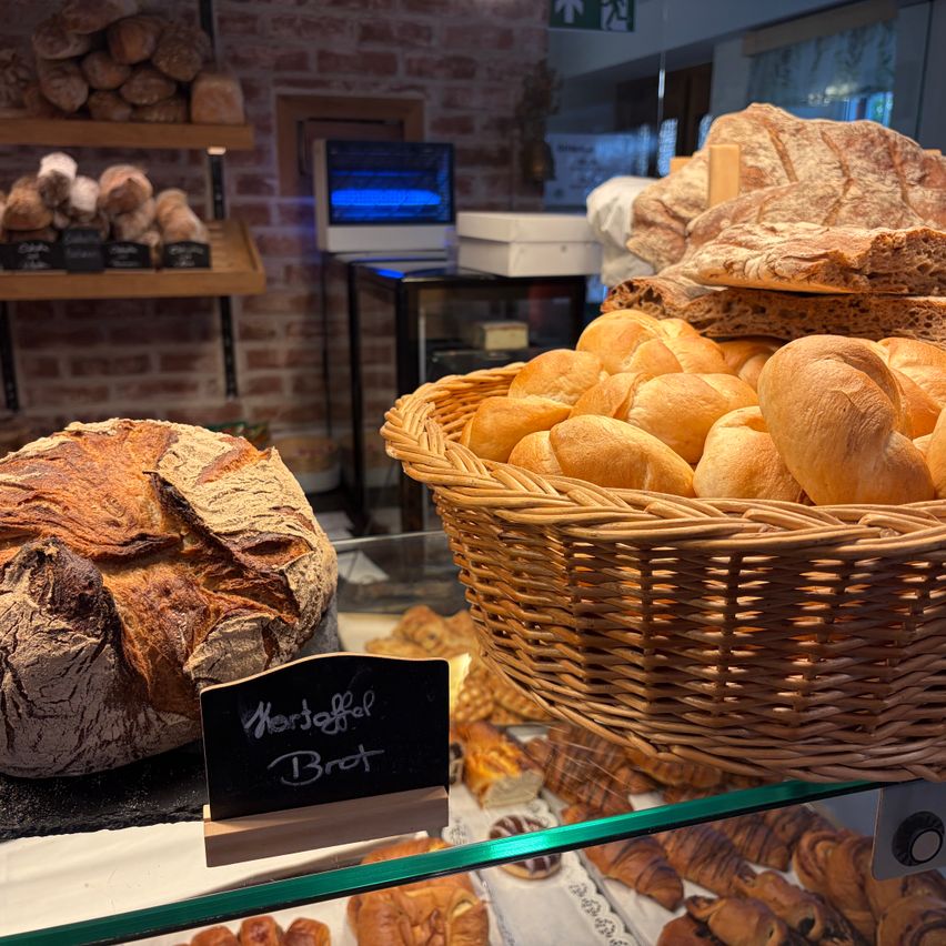 Eine Bäckerei-Vitrine mit einem großen Laib Brot, beschriftet mit 'Morgenfrisch Brot', und einem Korb mit kleineren Broten auf einem Glasregal.