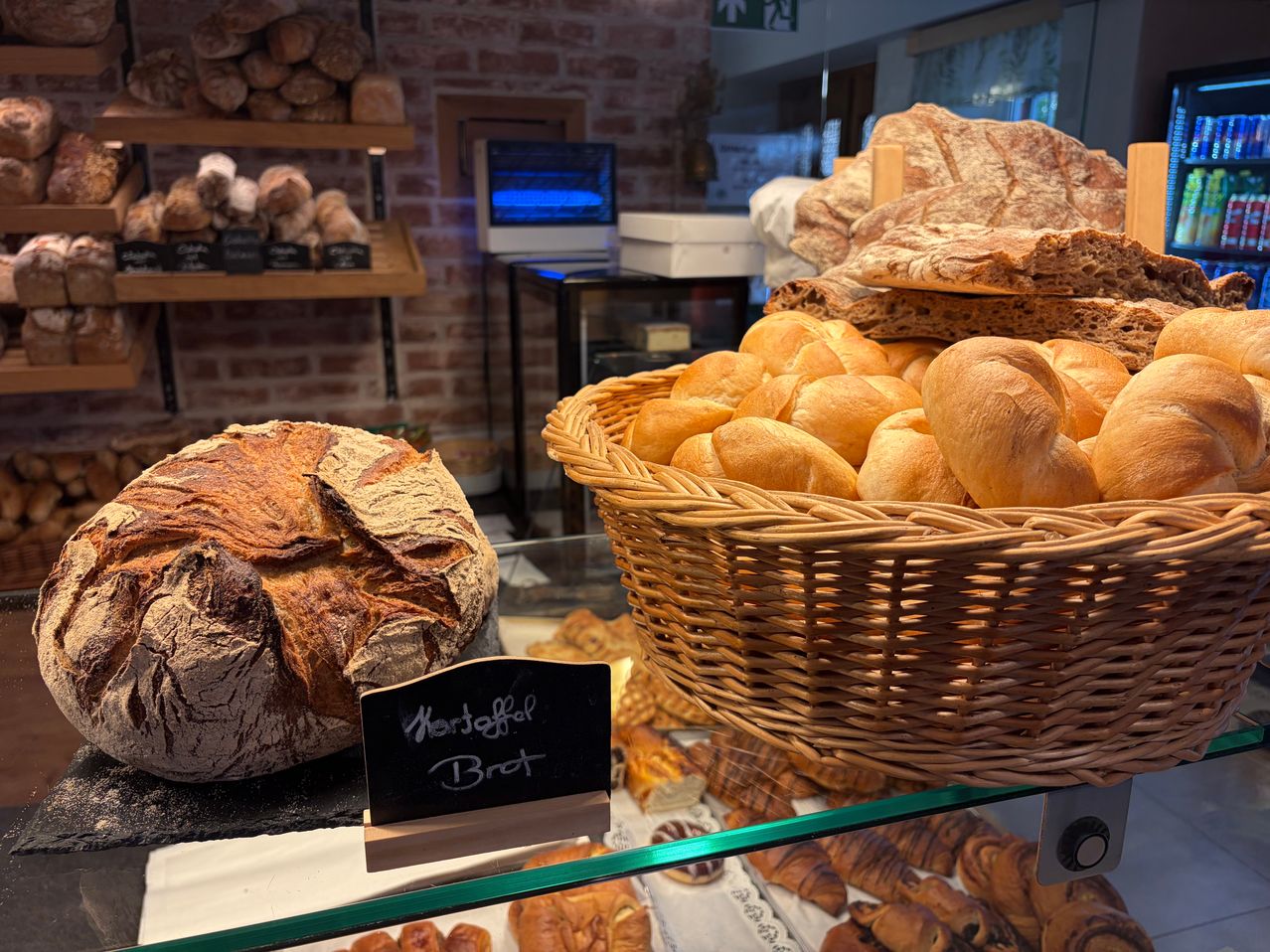 Eine Bäckerei-Vitrine mit einem großen Laib Brot, beschriftet mit 'Morgenfrisch Brot', und einem Korb mit kleineren Broten auf einem Glasregal.