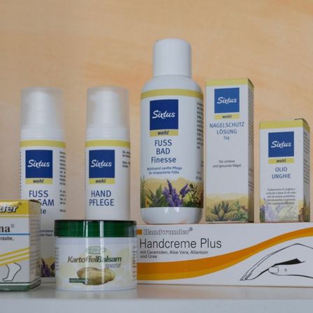 Eine Sammlung von Fußpflegeprodukten, einschließlich einer weißen Flasche Fußbad, einem grünen Topf Kartoffelcreme und einer weißen Box Handcreme Plus.