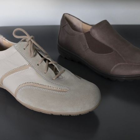 Zwei Paar Schuhe liegen auf einem dunklen Tisch. Eines ist beige mit Schnürsenkeln, das andere ist braun mit strukturierter Sohle.