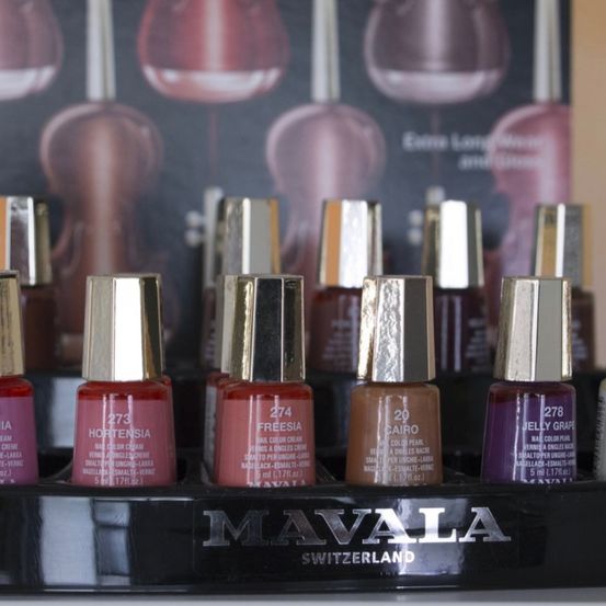 Eine Ausstellung von Mavala Nagellacken in verschiedenen Farben, einschließlich Hortensi, Freesia, Cairo und Jelly Grape. Die Flaschen befinden sich auf einem schwarzen Halter mit dem Markennamen Mavala und dem Herkunftsland Schweiz.