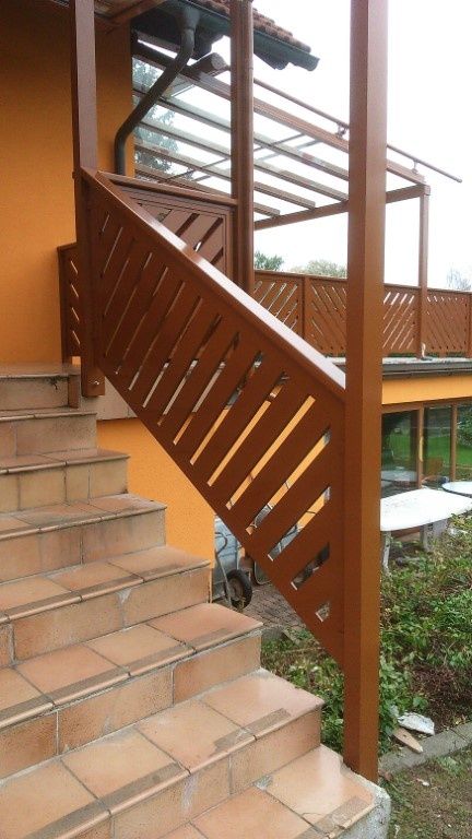 Eine Holztreppe mit braunen Geländern führt zu einem überdachten Balkon. Die Wände sind gelb gestrichen.