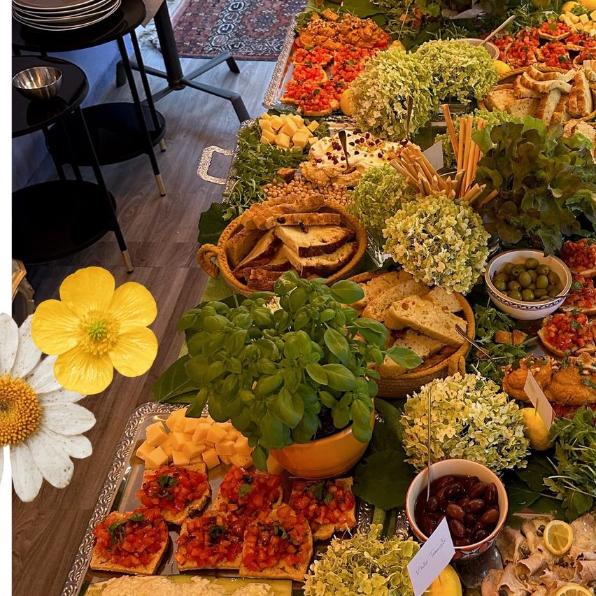 Ein Tisch gefüllt mit einer Auswahl an Lebensmitteln, einschließlich Brot, Gemüse und Käse. Blumen und eine Pflanze fügen Dekoration hinzu.