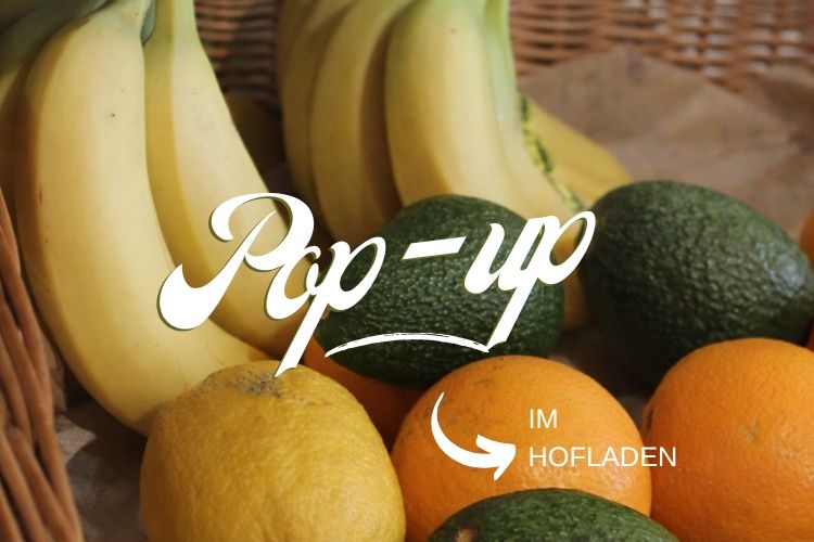 Ein Korb mit Früchten, darunter Bananen, Orangen und Avocados, mit einem 'Pop-up'-Text darauf.