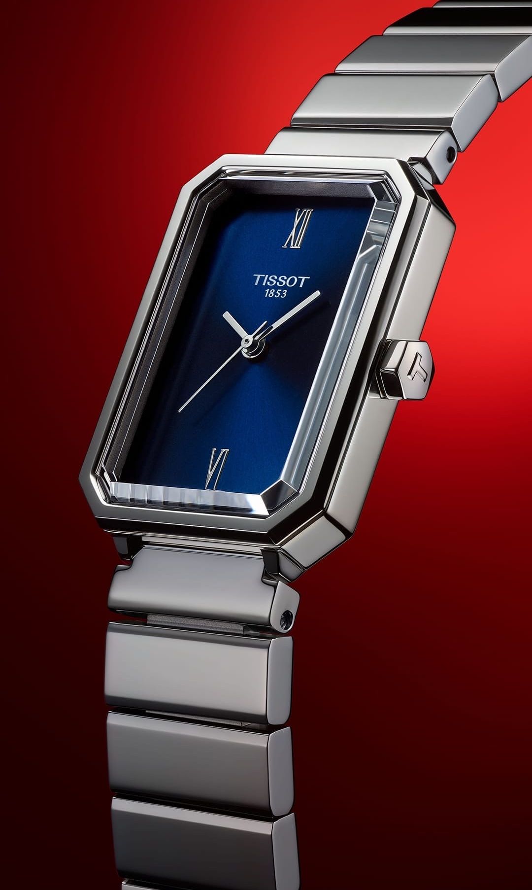 Eine Tissot-Armbanduhr mit blauem Zifferblatt und silbernen Akzenten vor rotem Hintergrund. Der Markenname und das Jahr '1853' sind auf dem Zifferblatt sichtbar.