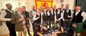 Gruppe von Menschen posiert vor einem Tisch mit Likörflaschen und Gläsern. Einige tragen Kilts. Schottische Flaggen sind im Hintergrund.