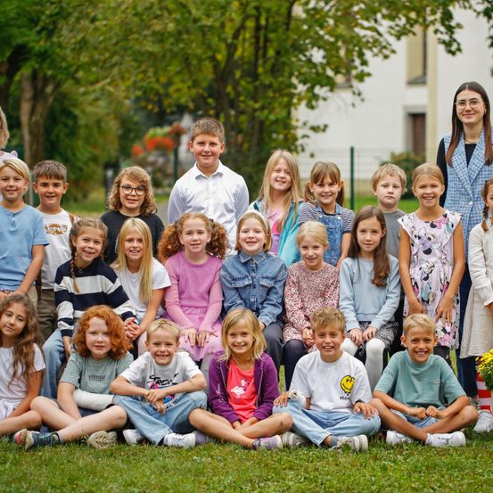 Eine Gruppe von Kindern in verschiedenen Kleidungsstücken posiert für ein Foto in einem Park mit einem Gebäude im Hintergrund.