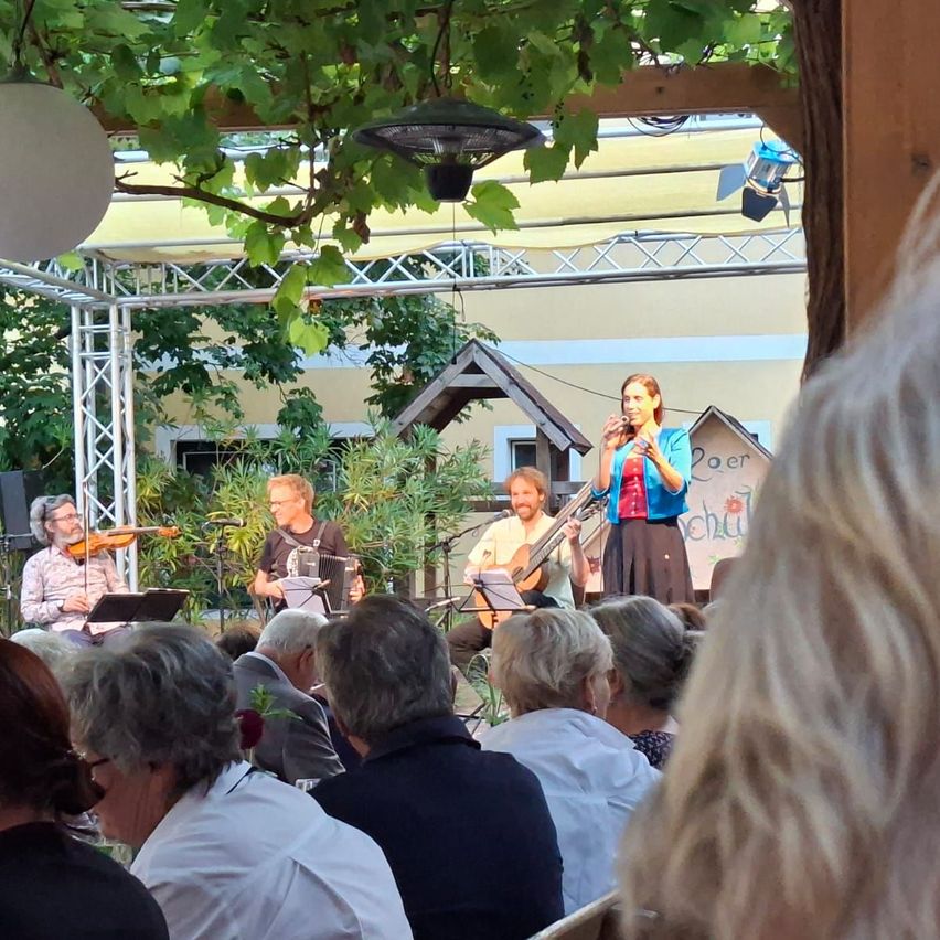 Eine Gruppe von Musikern tritt auf der Bühne auf, eine Frau singt, während ein Publikum älterer Erwachsener vorne zusieht.
