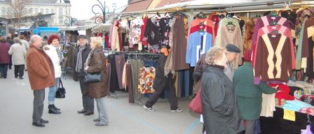 Mehrere Menschen stehen in einem Markt mit Kleidungsständen. Ein Mann geht in der Mitte.
