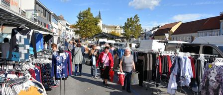 Ein Outdoor-Kleidermarkt mit vielen einkaufenden Menschen, verschiedenen Ständen mit ausgestellten Kleidungsstücken und einem klaren blauen Himmel.