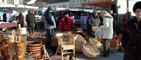Ein Markt mit mehreren Ständen, die Weidenkörbe und Möbel verkaufen, und Menschen, die herumlaufen. Im Hintergrund befinden sich Gebäude.
