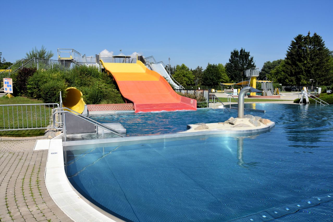 Freiluft-Wasserpark mit zwei bunten Rutschen, die zu einem großen Schwimmbecken an einem sonnigen Tag führen.