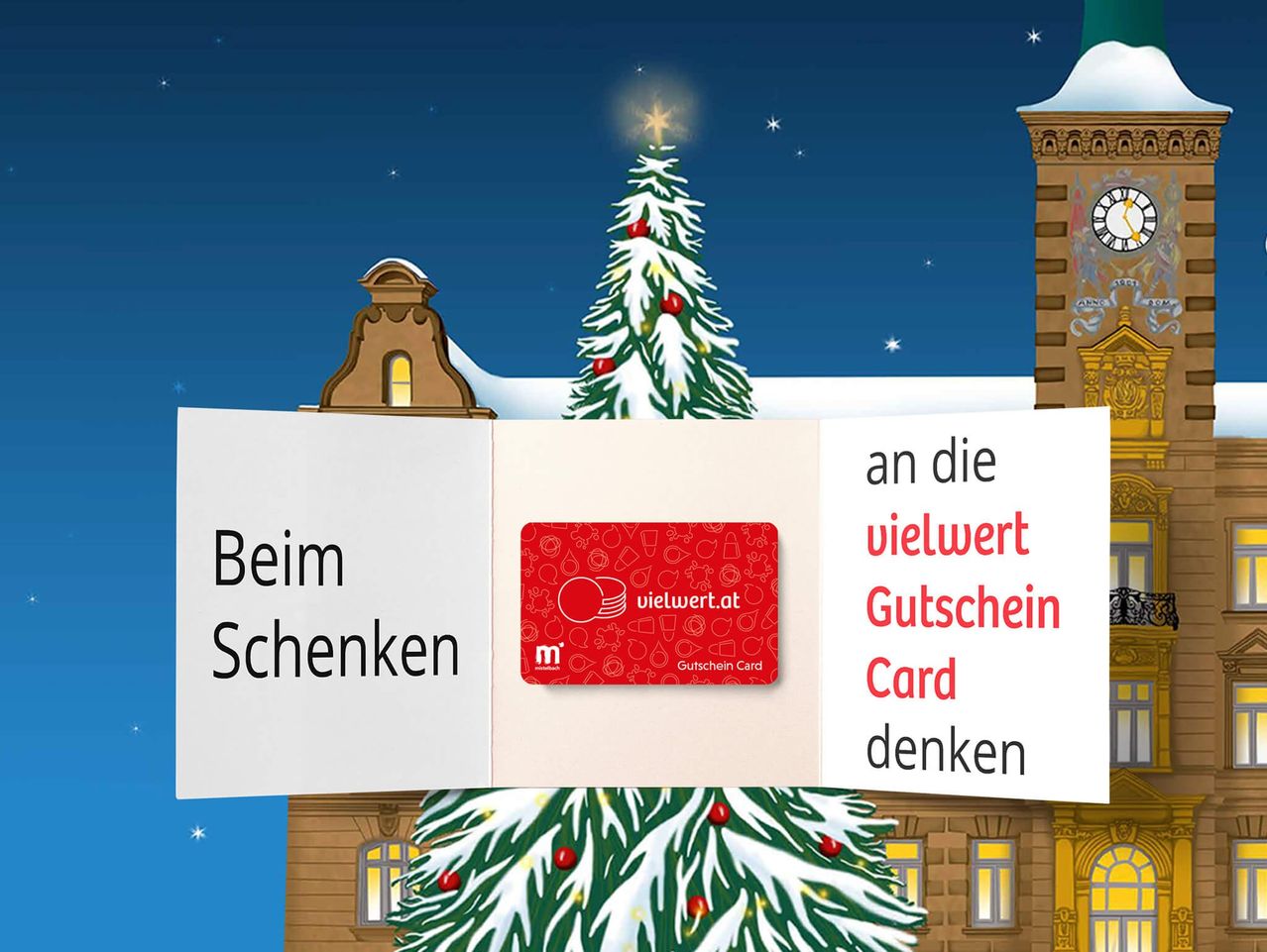 A Christmas tree stands outside a building with a tower, featuring a clock and a red gift card with the text 'vielwert Gutschein Card'. The image encourages thoughts of giving during the holiday season.
