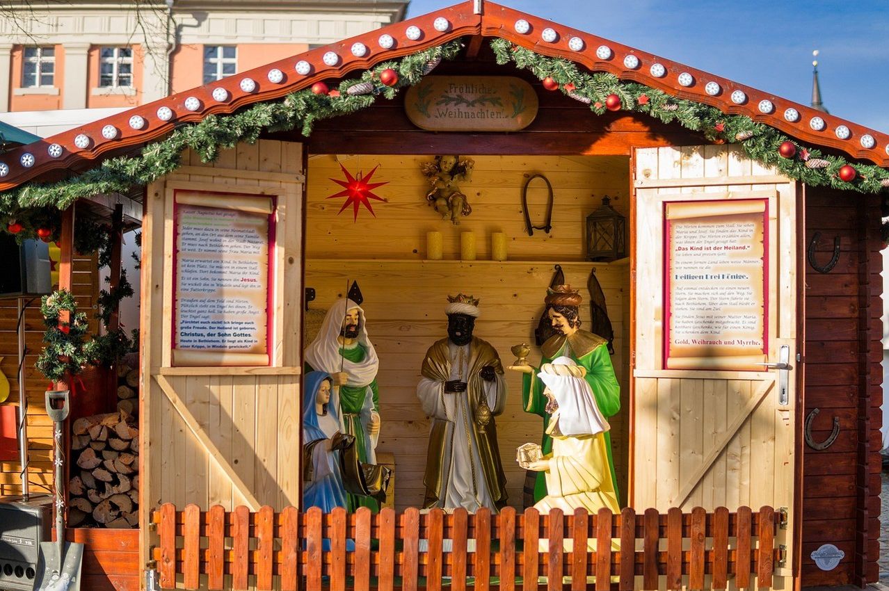Eine Krippe in einem Holzschuppen mit einem Weihnachtskranz, Weihnachtsdekoration und einem Schild, das 'Frohe Weihnachten' steht. Es zeigt Statuen von Maria, Josef und den drei Weisen.