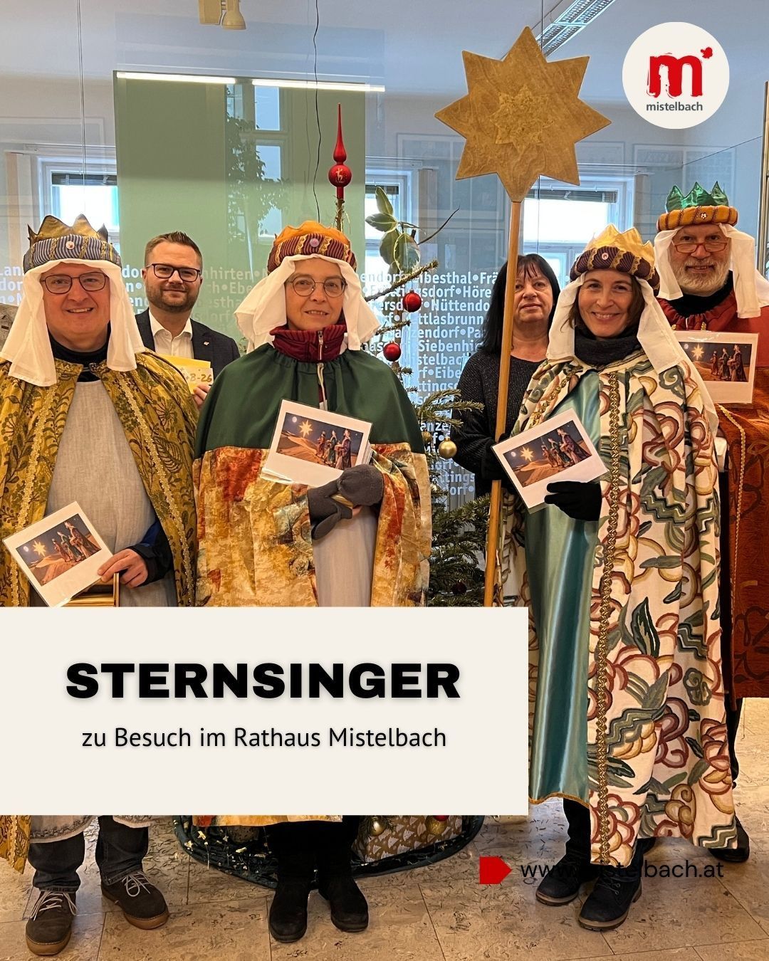 Eine Gruppe von Menschen, die als Weise Männer und Frauen gekleidet sind, halten einen Stern und Bilder in der Hand und stehen vor einem Weihnachtsbaum. Der Text 'STERNSINGER zu Besuch im Rathaus Mistelbach' steht auf dem weißen Hintergrund.