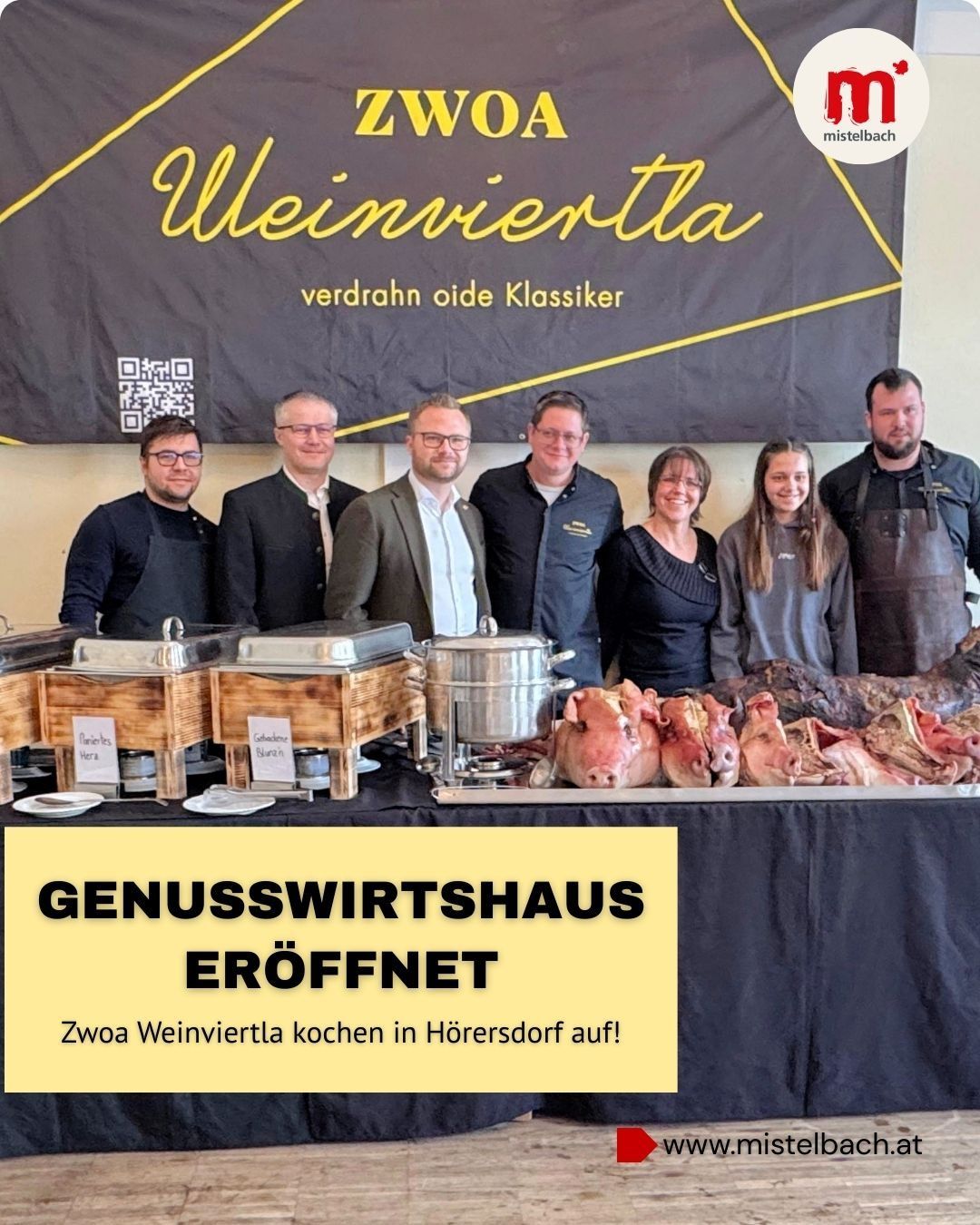 Mehrere Personen posieren für ein Foto vor einem Tisch mit Essen, hinter einem Banner, das 'ZWOA Weinviertler' sagt. Der Tisch hat Fleisch in einem silbernen Topf und Tabletts mit Essen. Das Banner sagt auch 'Genusswirtshaus Eroffnet'. Die Leute tragen formelle Kleidung.