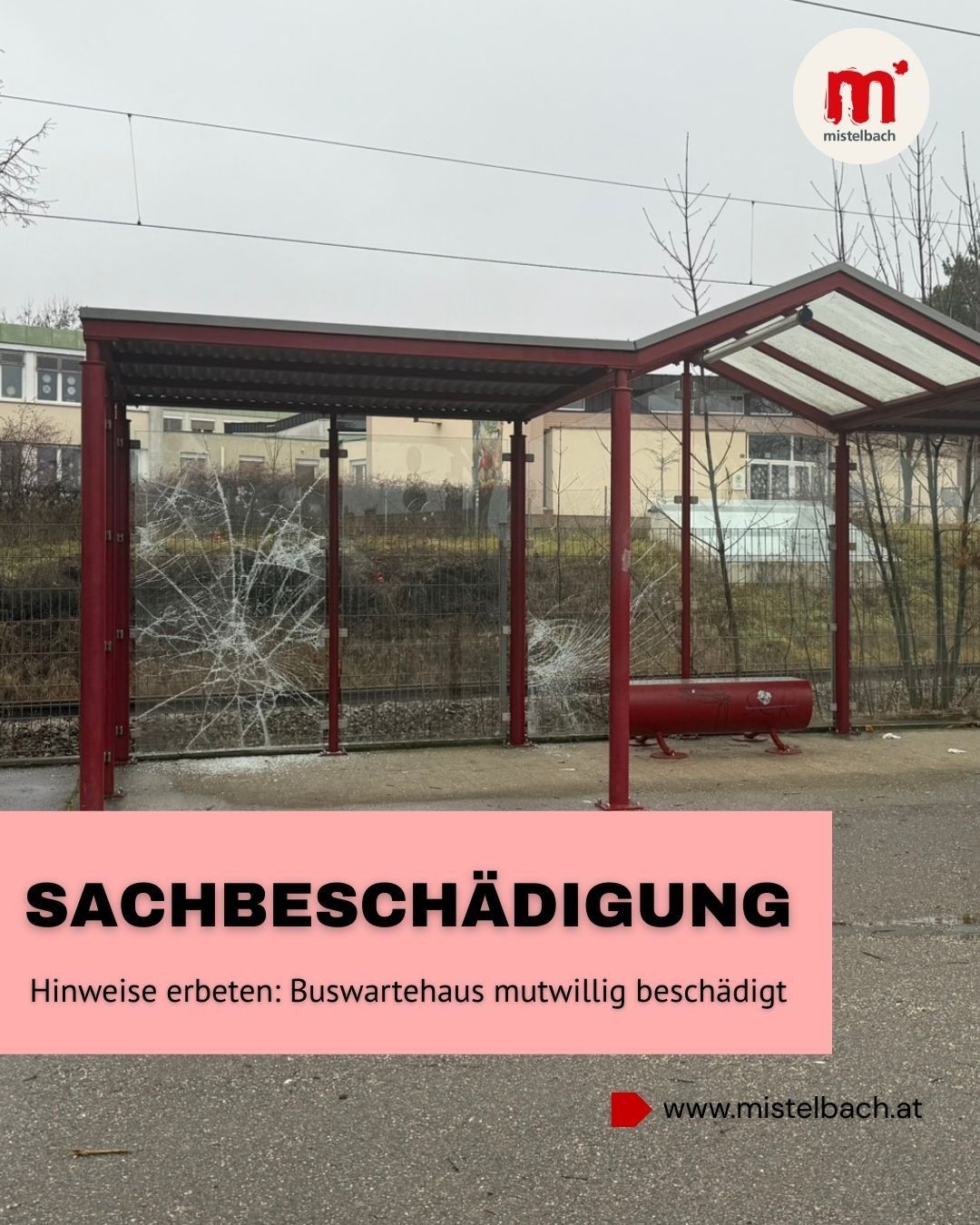 A vandalized bus stop with a broken glass window and a red tank. The sign reads 'SACHBESCHAEDIGUNG' and 'Buswartehaus mutwillig beschaedigt'. A building and a fence are in the background.
