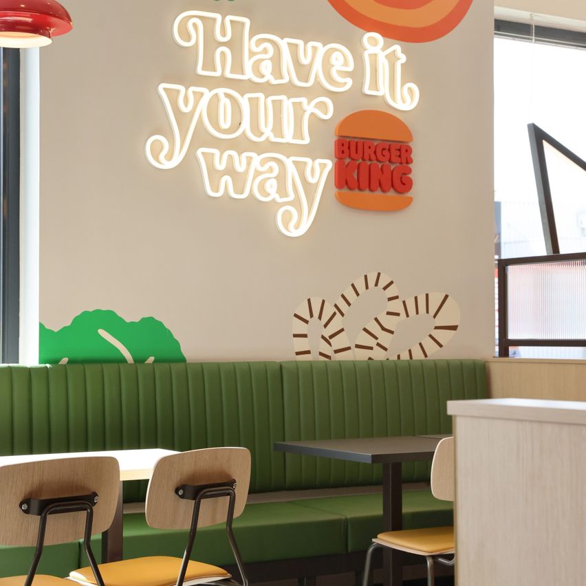 Das Innere eines Burger King Restaurants mit einem Neonschild, das 'Have it your way' sagt, und einer grünen Bankbestuhlung.