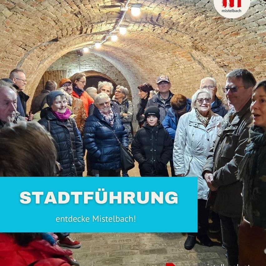 Eine Gruppe von Menschen ist in einem steingemauerten Tunnel versammelt. Ein blaues Schild mit weißer Schrift steht 'Stadtfuhrung entdecken Mistelbach!' Ein Wasserzeichen befindet sich in der oberen rechten Ecke.