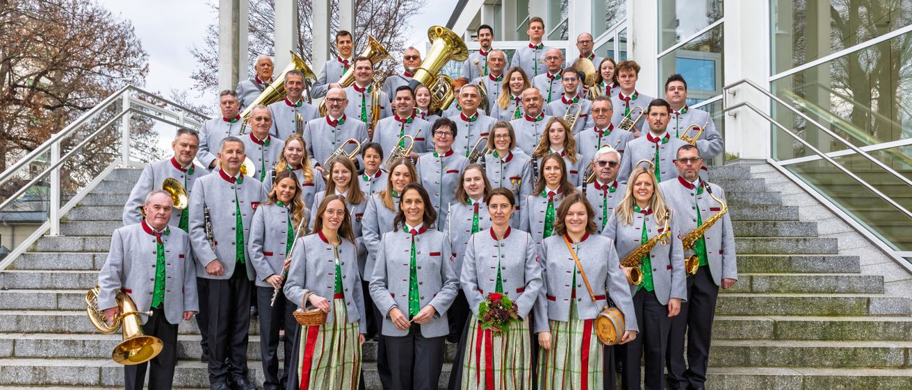 Eine Gruppe von Musikern in gleichen Uniformen, die verschiedene Instrumente halten, posiert für ein Foto auf einer Treppe.