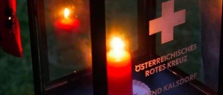 Eine Laterne mit einer brennenden Kerze im Inneren und einem roten Kreuz-Symbol. Der Text 'Osterreichisches Rotes Kreuz' und 'Friedenslicht' steht auf der Laterne.
