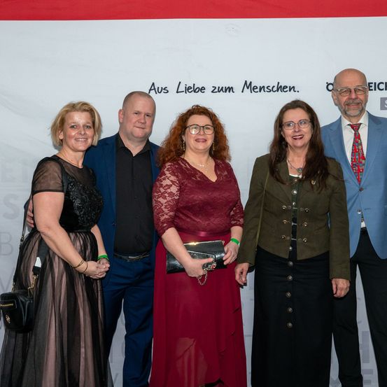 Fünf Personen posieren für ein Foto vor einem Banner mit deutschem Text. Sie tragen alle formelle Kleidung.