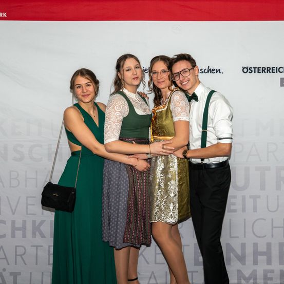 Vier Personen posieren für ein Foto. Zwei Frauen tragen traditionelle Kleider. Eine Frau hat eine Brille und eine Halskette. Ein Mann mit Brille und Hosenträger hält die Taille der Frau in der Mitte.