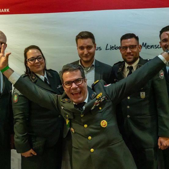 Eine Gruppe von Militärangehörigen, die lächelnd für ein Foto posiert, mit einem Banner im Hintergrund.