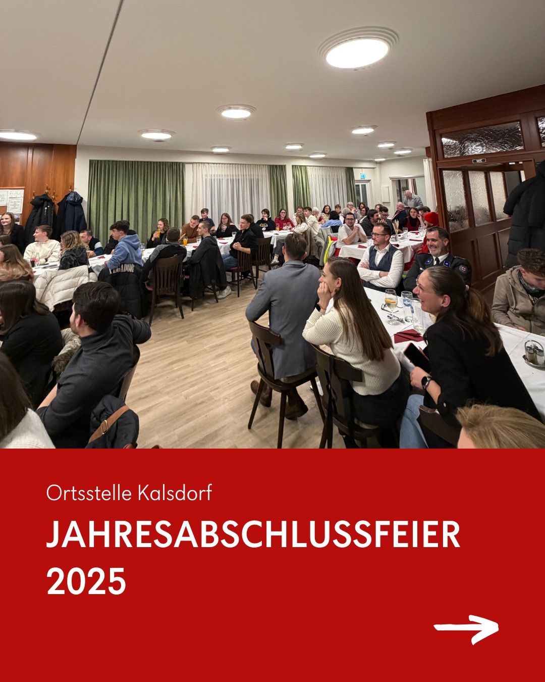 Eine große Gruppe von Menschen sitzt um Tische in einem Raum. Ein roter Banner am unteren Rand sagt Jahresabschlussfeier 2025.