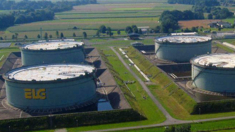 Luftaufnahme eines Industriegeländes mit vier großen zylindrischen Lagertanks, zwei davon mit den Buchstaben ELY deutlich sichtbar. Das Gelände ist von grünen Feldern und einem klaren blauen Himmel umgeben.