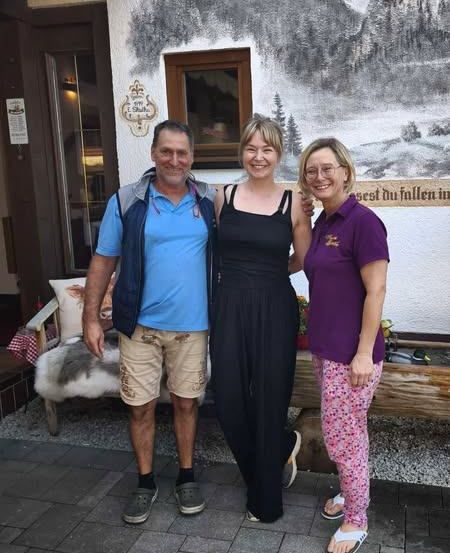 Drei Menschen lächeln und stehen vor einem Gebäude mit einem Wandbild an der Wand.