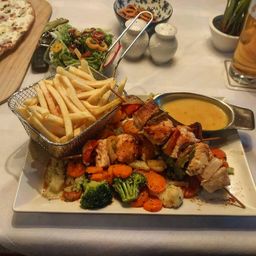 Ein Gericht mit Kebabs, gegrilltem Gemüse und Pommes Frites mit Salat, Pizza und Sauce auf einem Tisch.