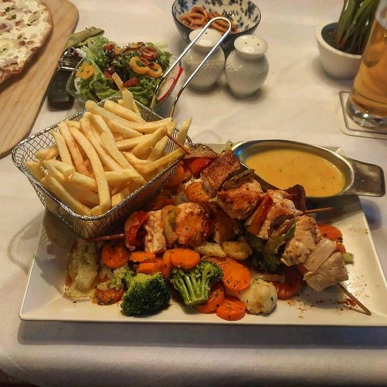 Ein Gericht mit Kebabs, gegrilltem Gemüse und Pommes Frites mit Salat, Pizza und Sauce auf einem Tisch.