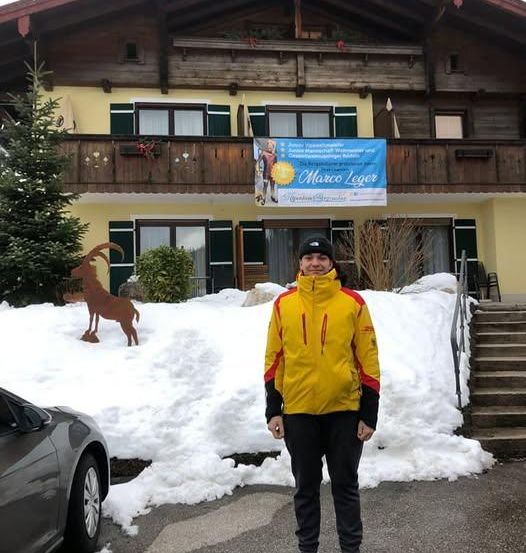 Ein Mann steht vor einem schneebedeckten Haus mit einem Banner mit der Aufschrift Marco Leger.