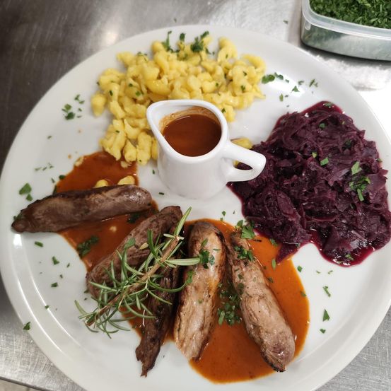 Ein weißer Teller mit einem Gericht aus Fleisch, Kartoffelpüree und Rotkohl. Das Fleisch ist mit einer Sauce überzogen.
