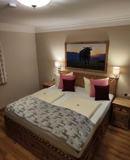 Ein Schlafzimmer mit einem großen Bett, geschmückt mit dekorativen Kissen, über dem ein Gemälde einer Kuh hängt.