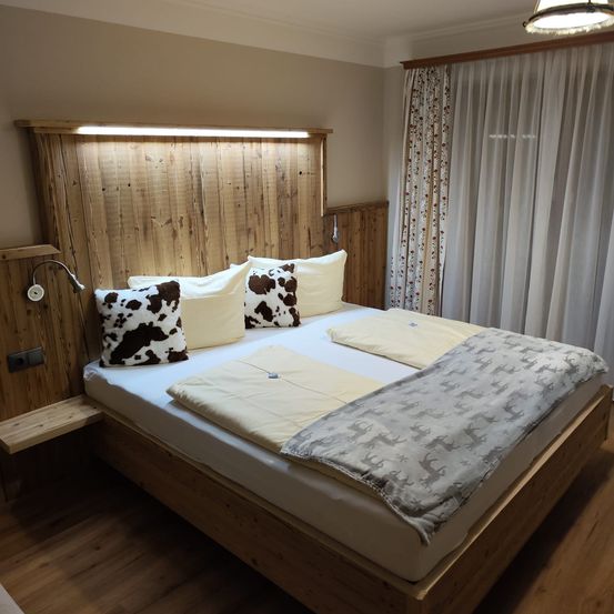 Ein Schlafzimmer mit einem Holzbett, Kuhfellkissen, einer Decke und Vorhängen.