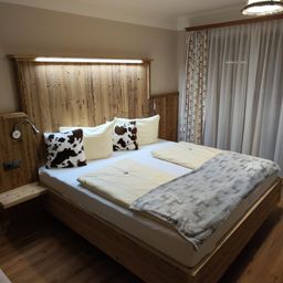 Ein Schlafzimmer mit einem Holzbett, Kuhfellkissen, einer Decke und Vorhängen.